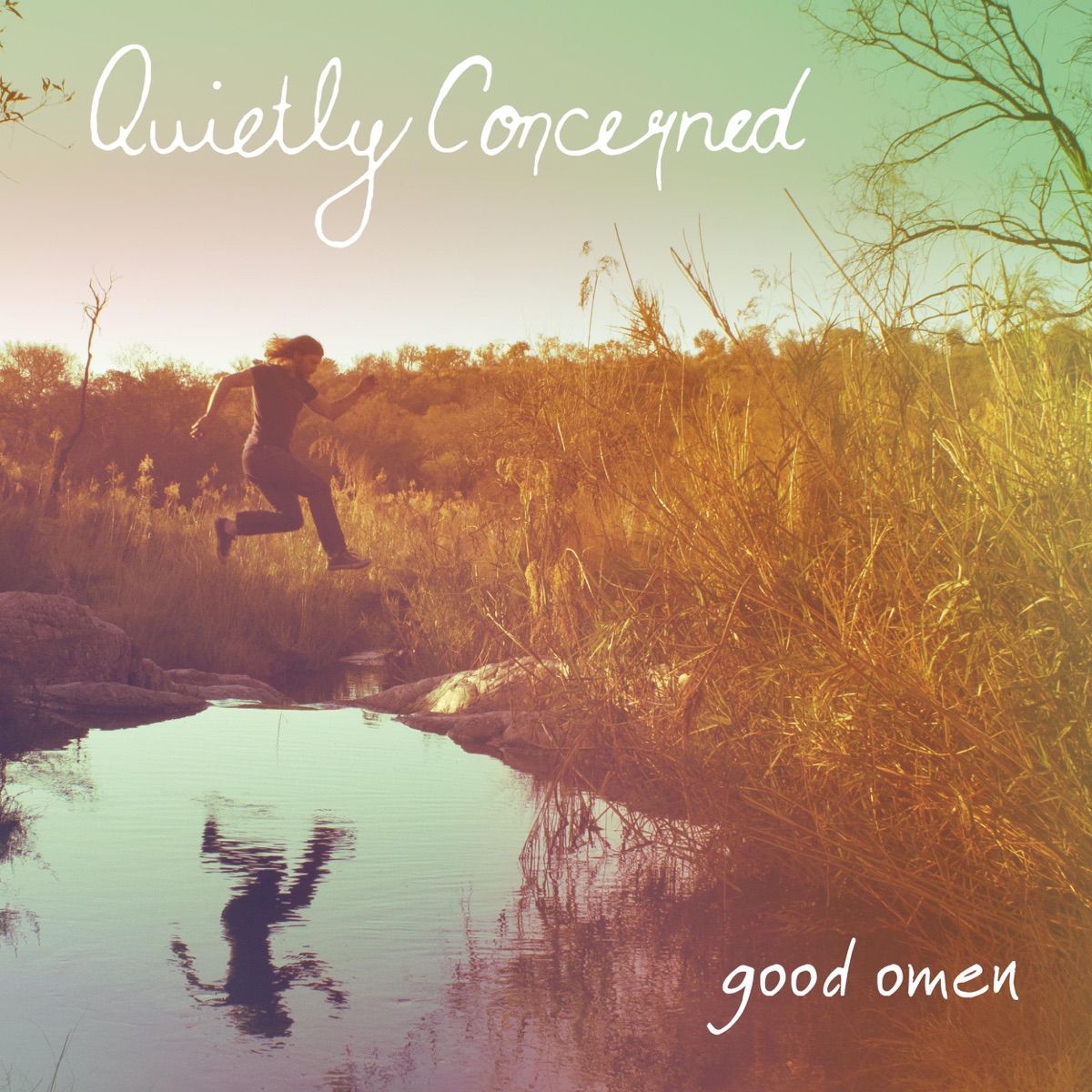 Good Omen single cover. A long-haired man leaps across a stream through tall golden grass at sunset, his reflection in the water below. "Quietly Concerned" and "good omen" are written in white handwriting.